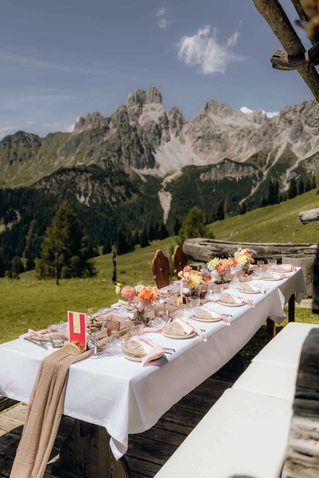 Ein gedeckter Tisch mit frischen Blumen steht vor der alpinen Bergkulisse bei eurer Hochzeit.