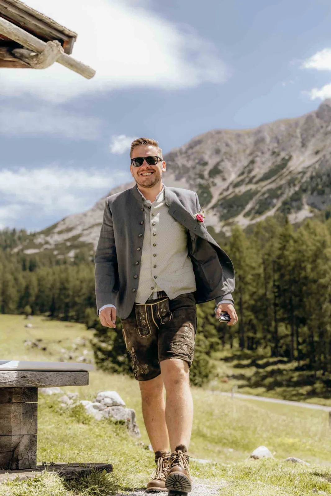 Der Bräutigam läuft lächelnd in traditioneller Tracht über eine Almwiese bei diesem Elopement, festgehalten von eurem Hochzeitsfotograf München.