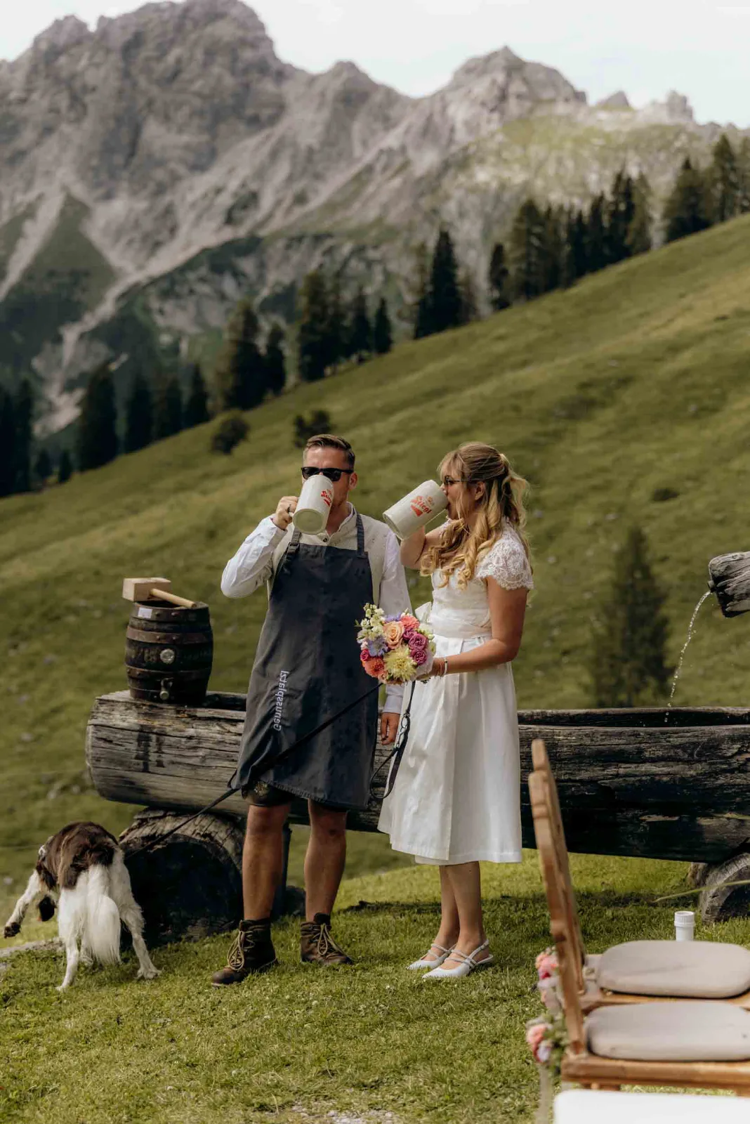 Hochzeitsfotograf München begleite ich Brautpaare wie diese beiden bei ihrem Elopement in Österreich auf der Alm mit einem gemeinsamen Anstoßen aus Bierkrügen.