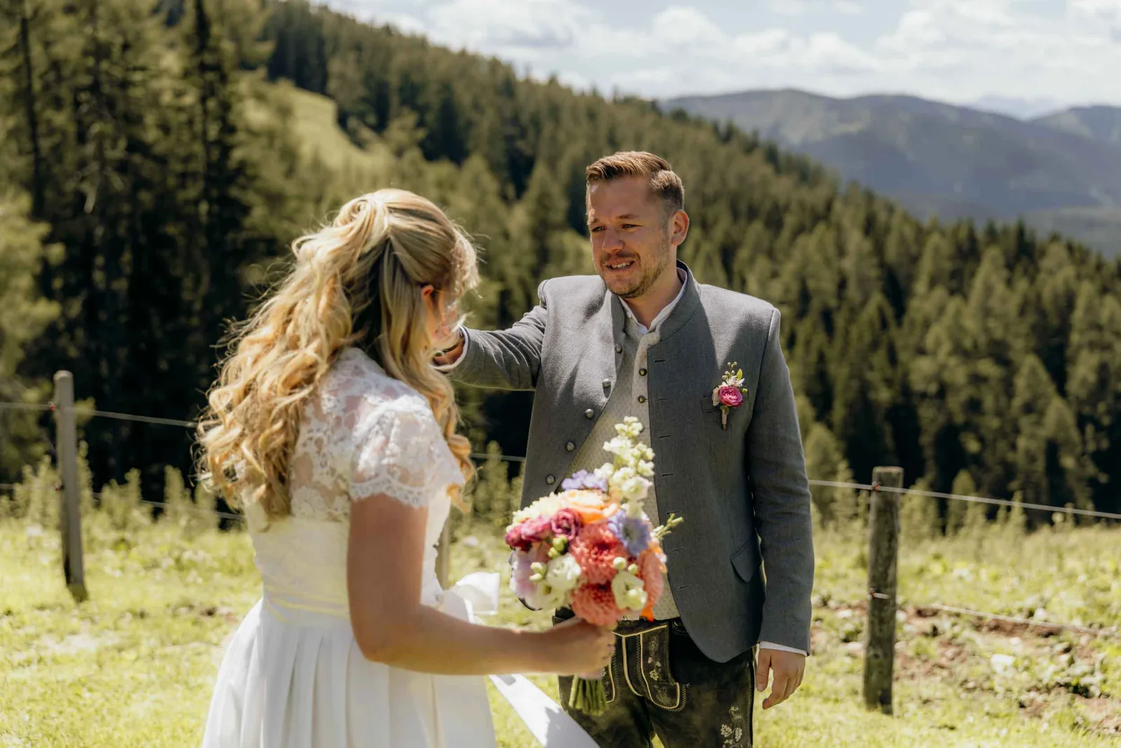 Ein Brautpaar hält inne beim First Look, während ich als Hochzeitsfotograf München diesen persönlichen Moment auf einer sonnigen Bergwiese mit der Kamera festhalte.