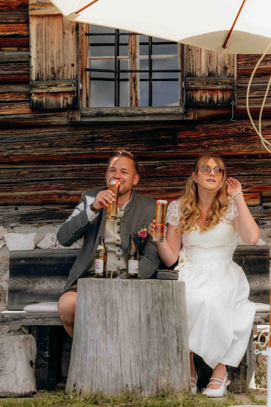 Das Brautpaar trinkt an einem Holztisch vor der Löckenwaldhütte entspannt ein kühles Bier.