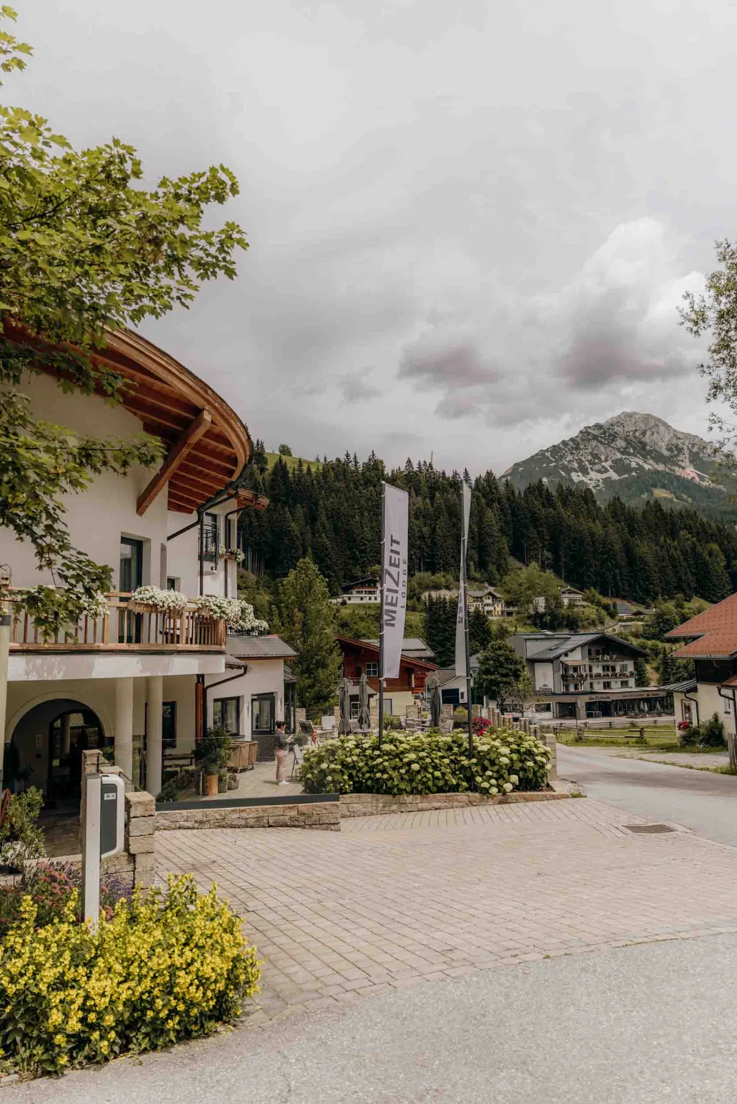 Ein Hotelgebäude in Filzmoos zeigt sich bei bewölktem Himmel vor einer alpinen Berglandschaft.