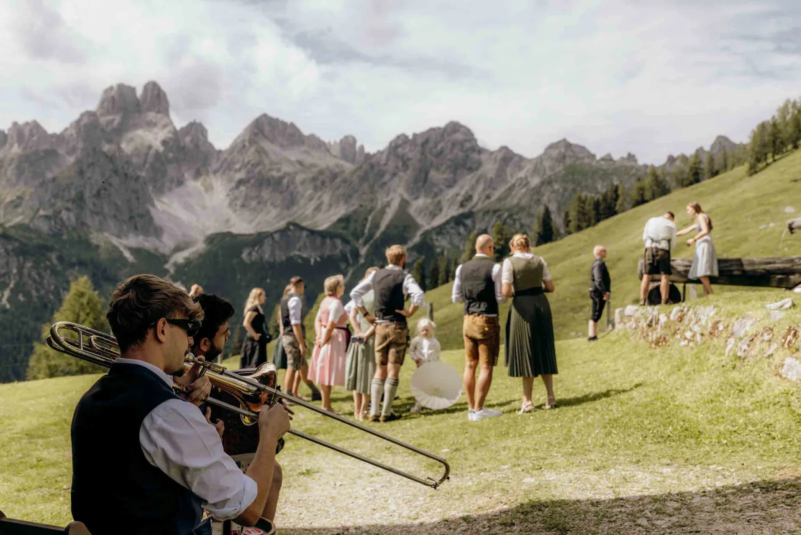 Musiker spielen auf einer Alm in Filzmoos, während Gäste im Hintergrund auf der Wiese stehen.
