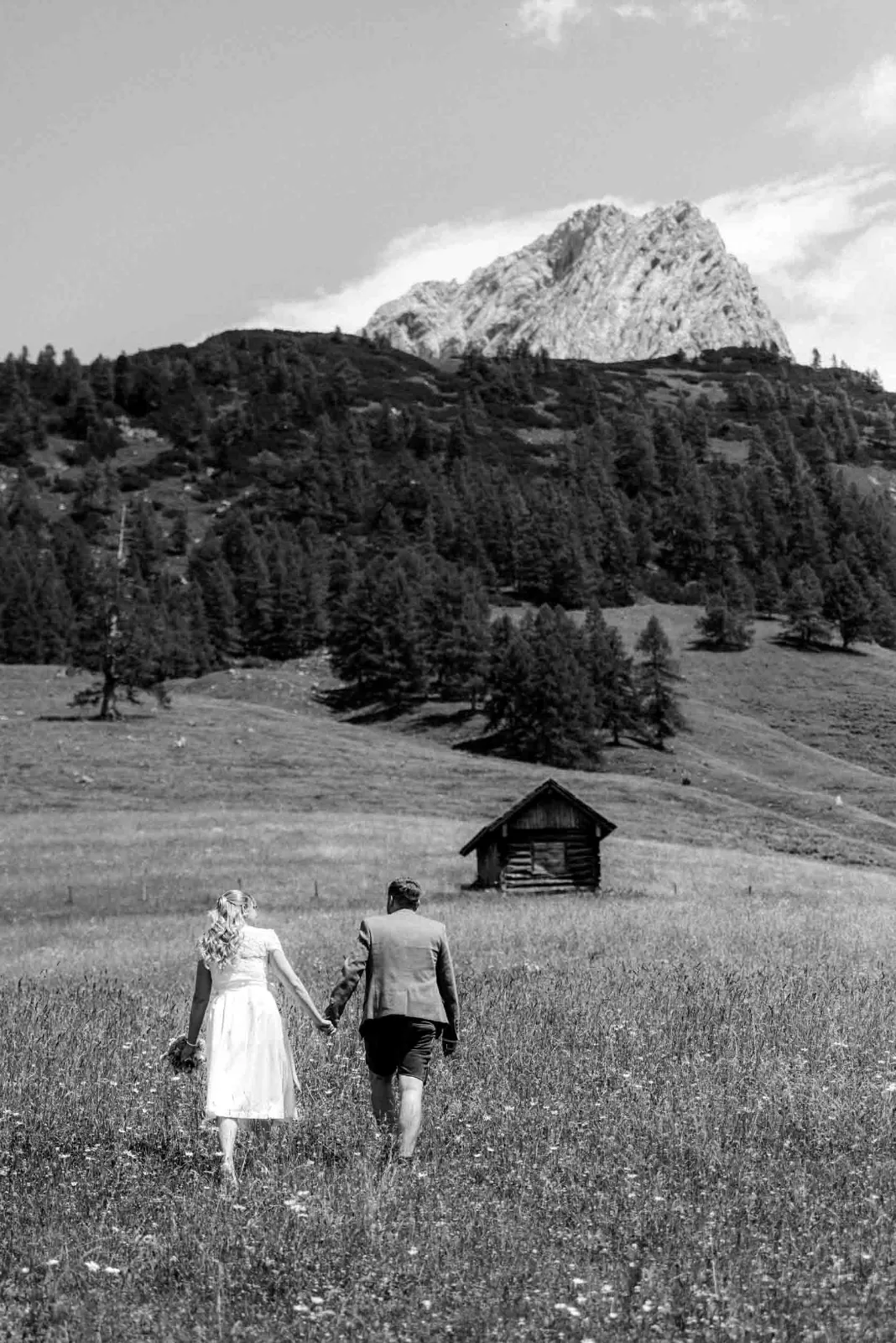 Ein Paar geht Händchen haltend über eine Wiese, begleitet von mir als Hochzeitsfotograf München bei einem Elopement in den Bergen.
