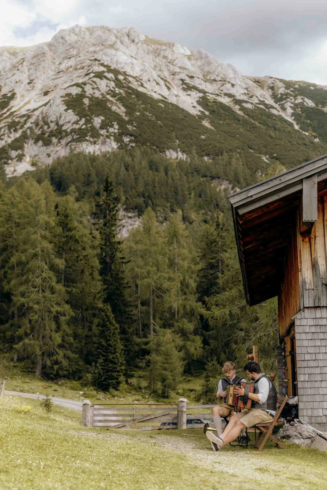 Zwei Musiker spielen vor einer Hütte in den Bergen auf ihren Instrumenten, festgehalten von eurem Hochzeitsfotograf München.