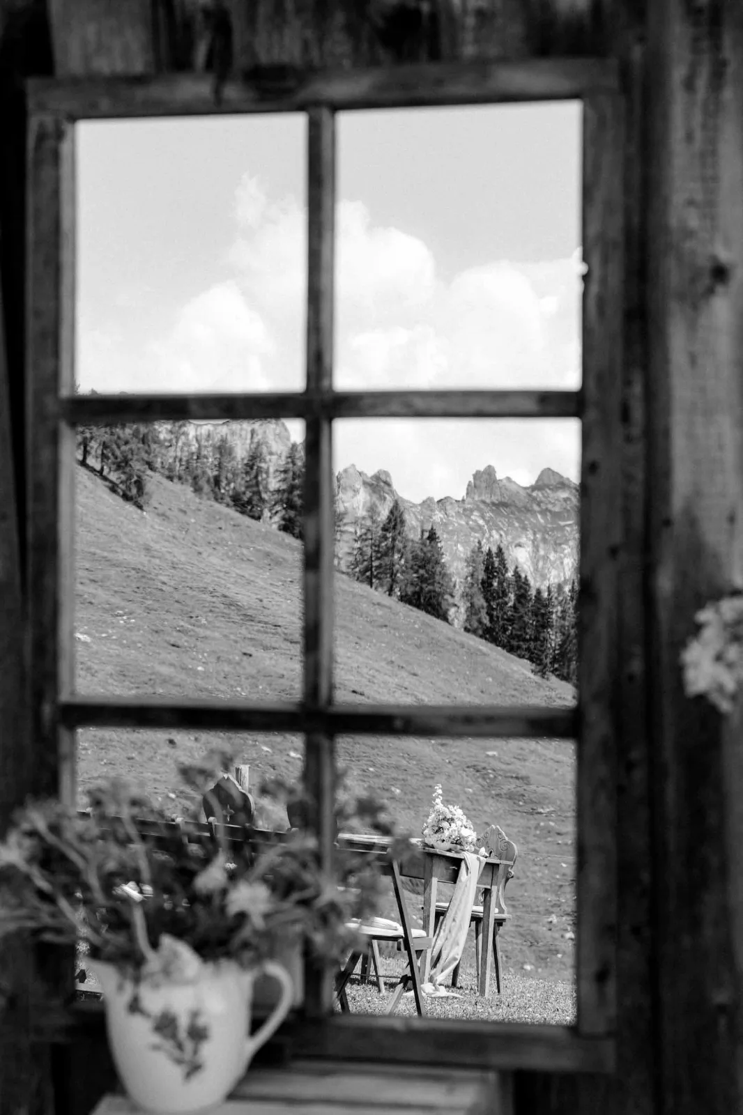 Der Blick durch ein altes Holzfenster auf die gedeckte Tafel vor den Bergen.